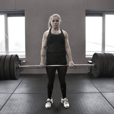 Sanne Visser doet in een sportschool een deadlift. Ze heeft het gewicht tot haar heup en staat rechtop.