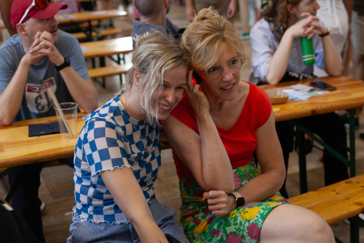 Twee zittende bezoekers, ogenschijnlijk moeder en dochter, die een koptelefoon delen om een lezing te volgen.