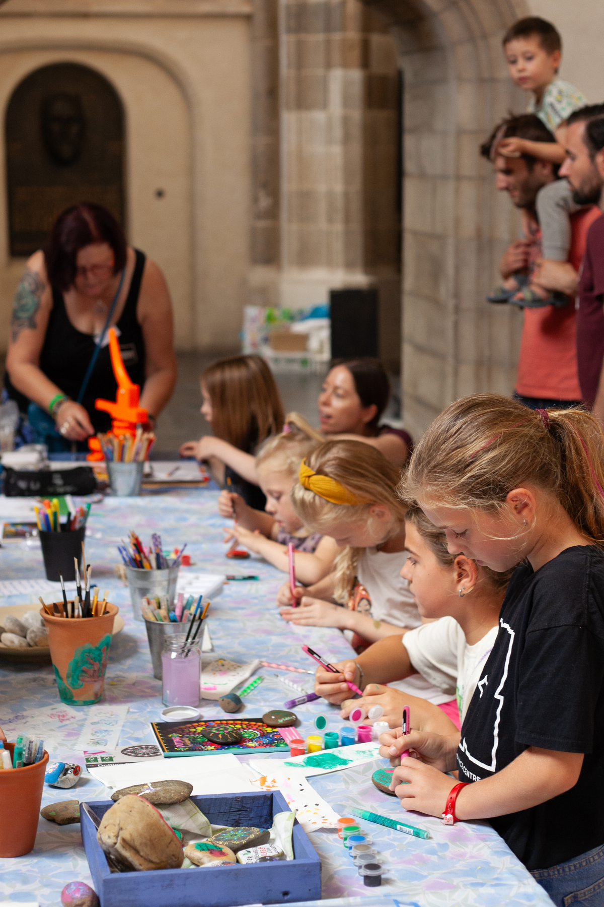 Een lange tafel met knutselspullen en kinderen, vaders en NVV vrijwilliger Ruth.